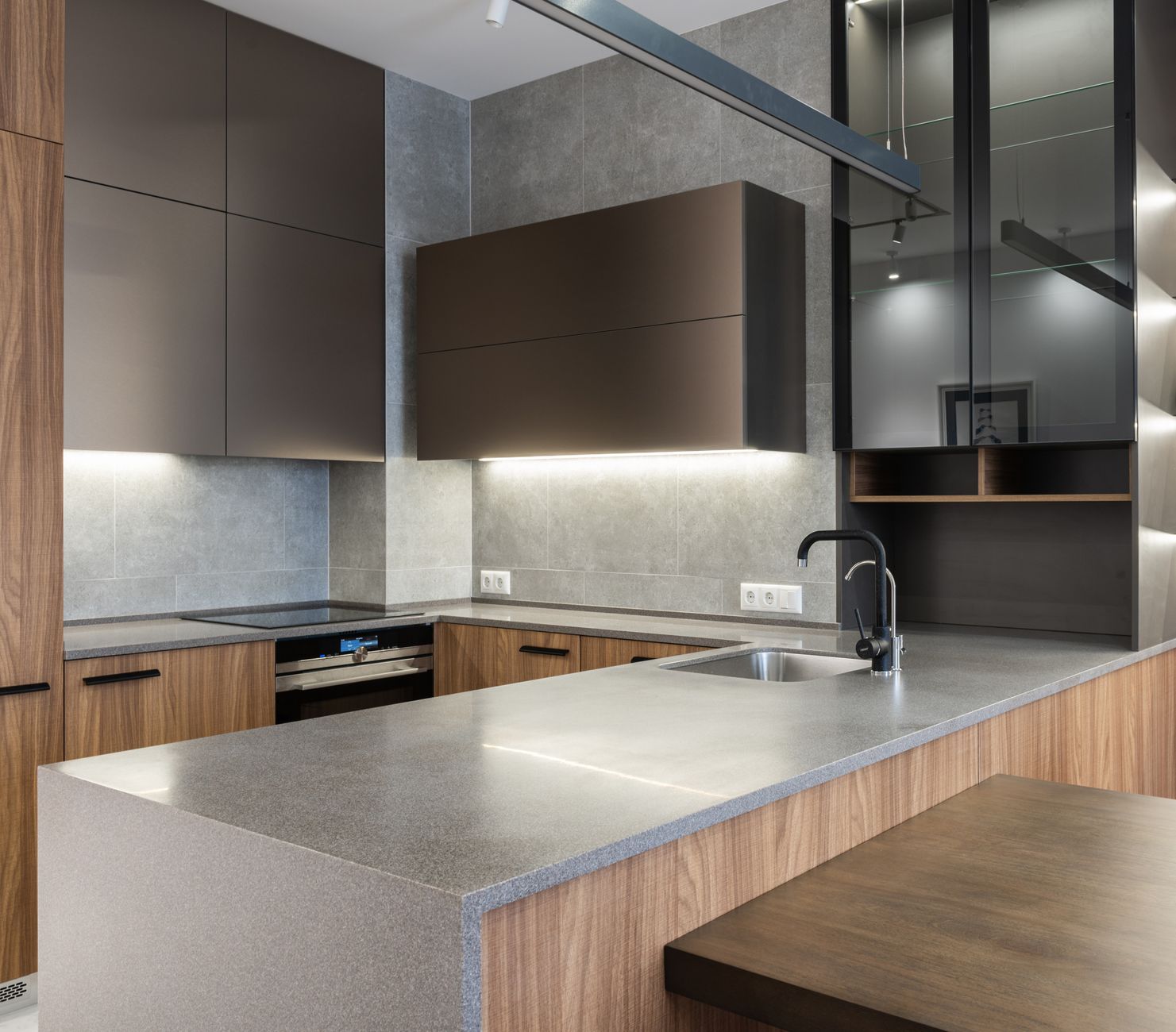 Interior of modern kitchen with faucet on gray counter and cupboards with illumination near electric cooker in contemporary apartment at home