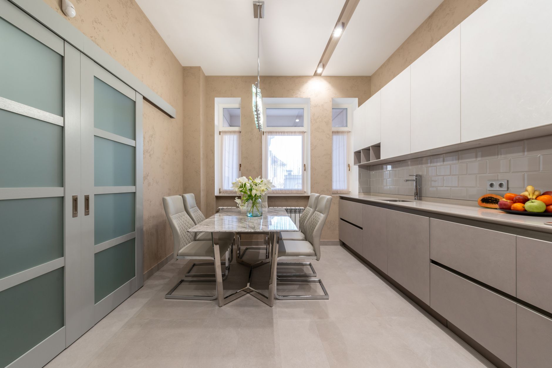 Modern kitchen interior with minimalist cabinets and marble dining table with chairs next to glass doors and window