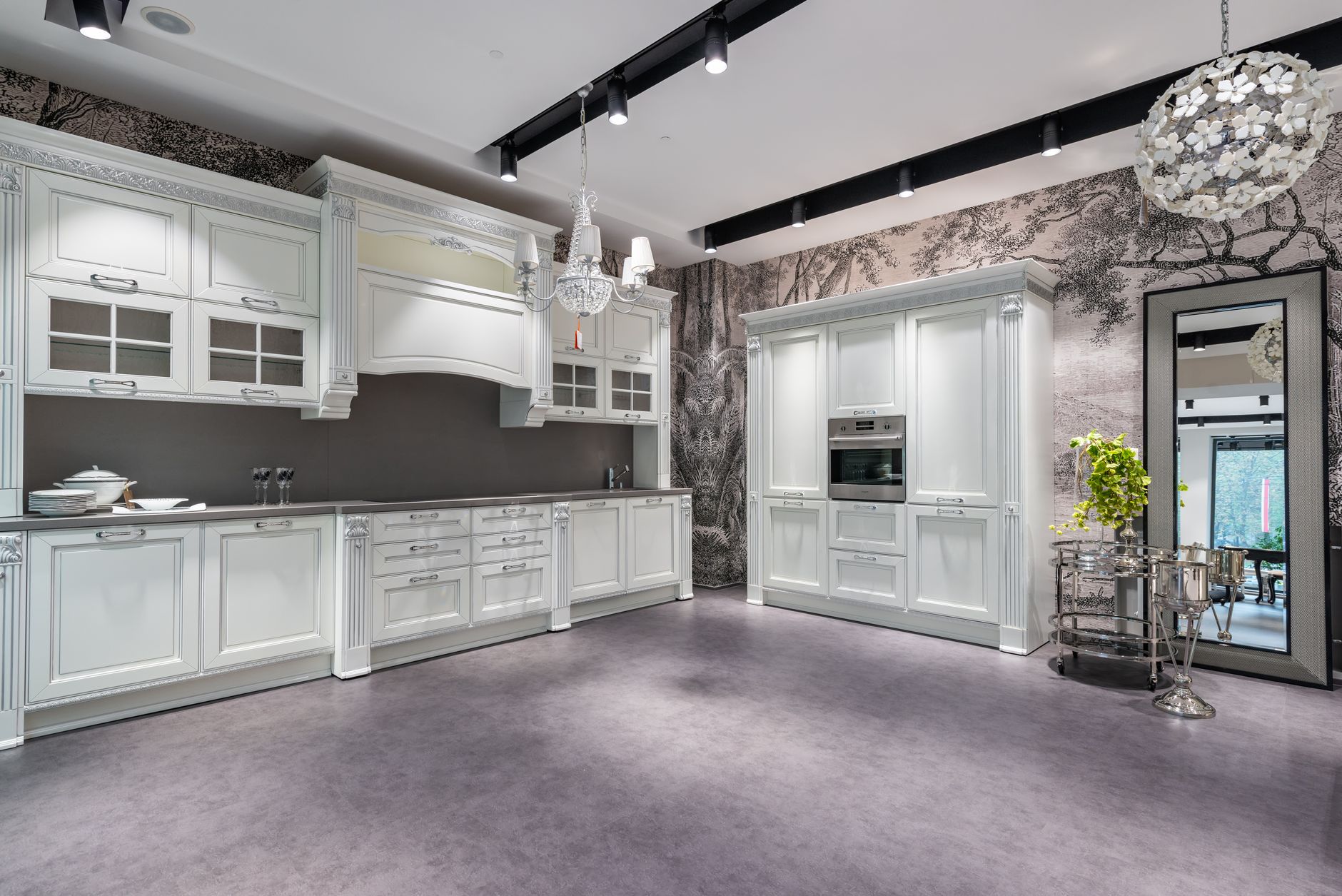 White cabinets with dishware in spacious stylish kitchen with oven and side table near window and potted plant in apartment