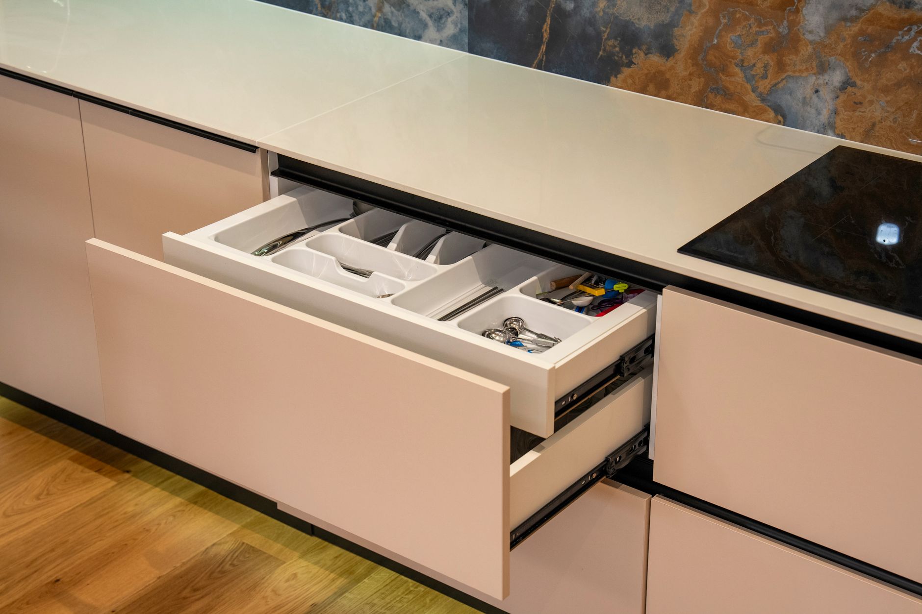 Open kitchen drawer in modern kitchen with organized cutlery and utensils.