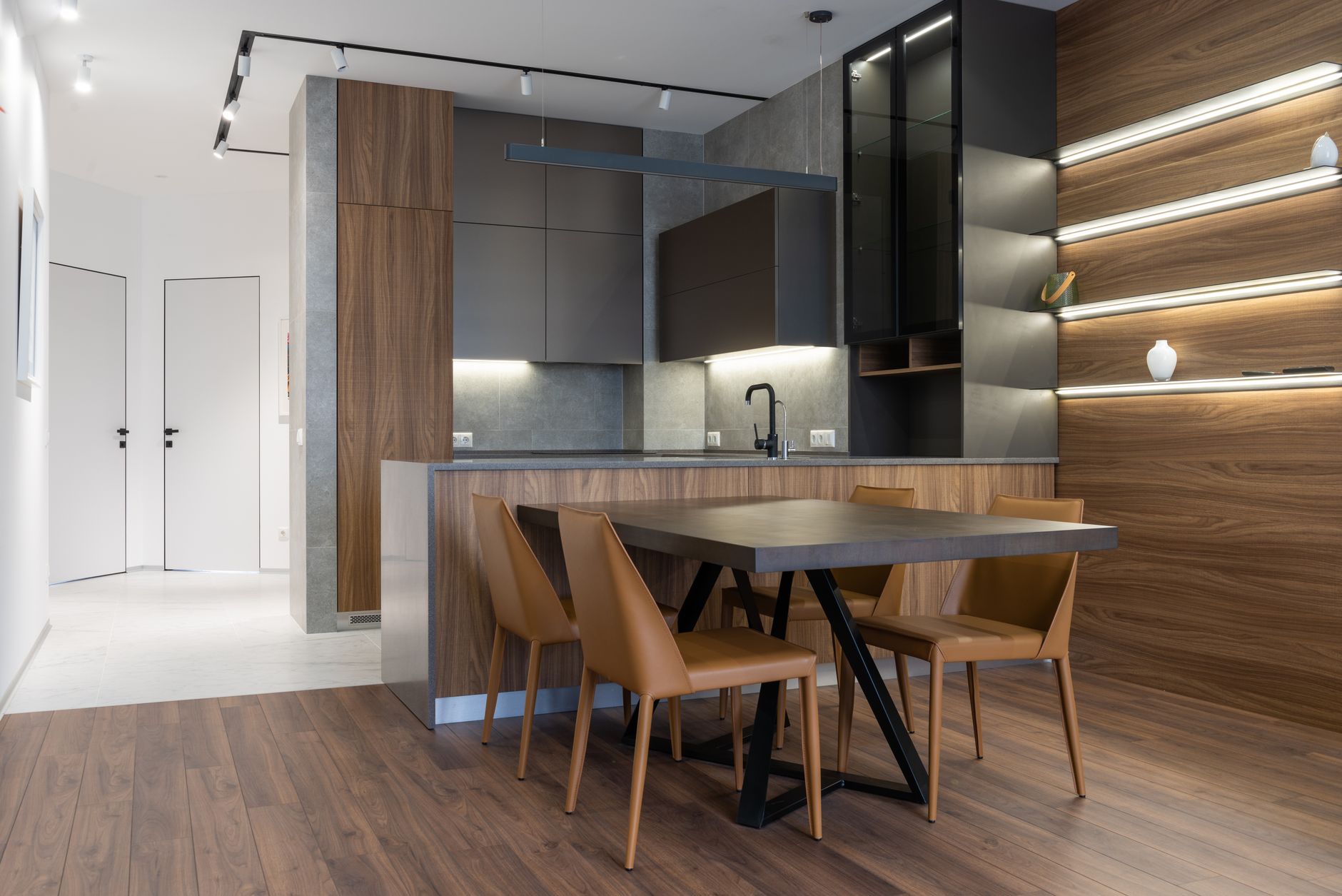 Table and chairs placed near modern kitchen counter with cupboards in stylish apartment with white doors in corridor at home